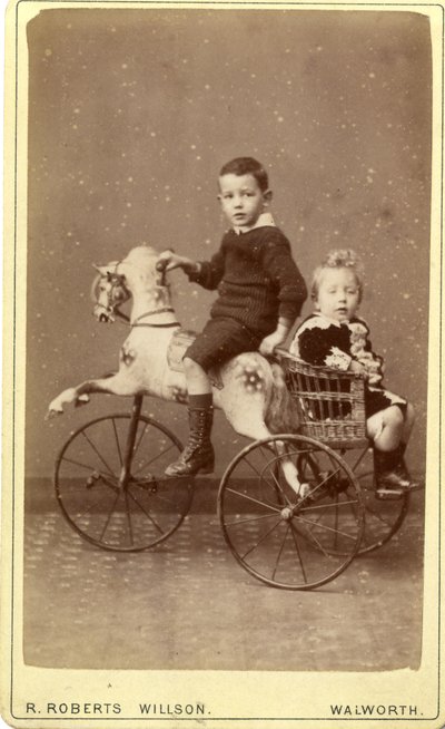 Jonge jongen op hobbelpaard met jong meisje in rieten wagen erachter, 1880s (albumineprint) door R. Roberts Willson